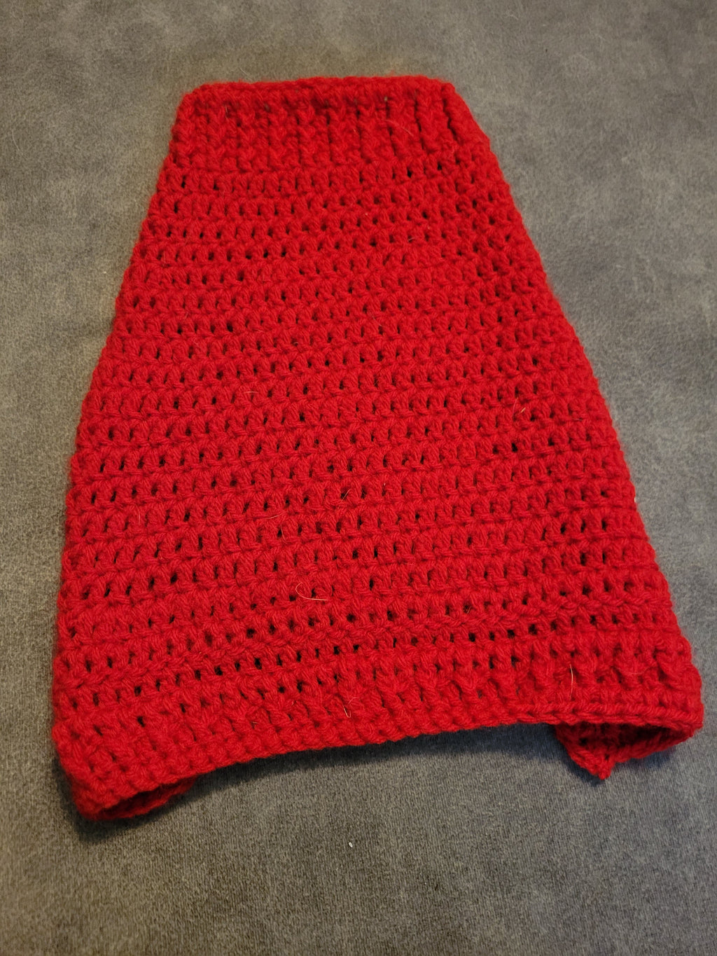 Red knitted puppy sweater laid flat on gray fabric.