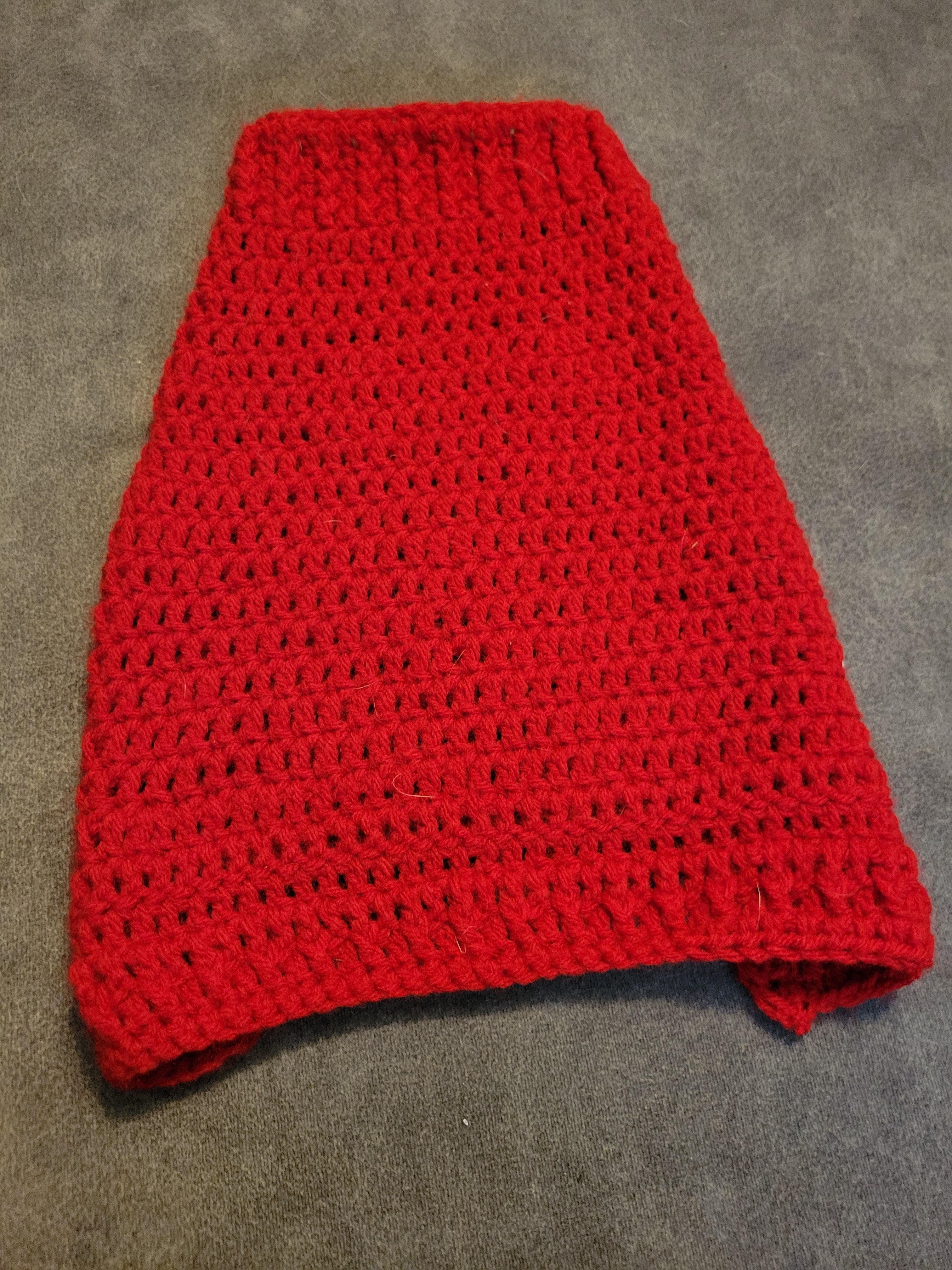 Red knitted puppy sweater laid flat on gray fabric.